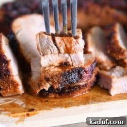 Quick and Tender Air Fryer Pork Tenderloin 10 A fork piercing a stack of two perfectly cooked pieces of pork tenderloin on a rustic wood cutting board, highlighting its succulent interior.