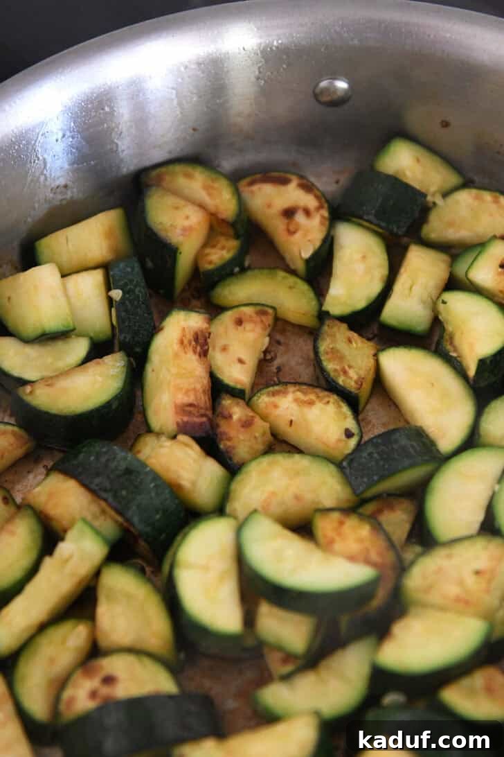 Effortless Tuna Zucchini Orzo Skillet 3 Close-up of golden-brown zucchini pieces sautéing in olive oil within a stainless steel skillet, showing the beginning of the cooking process.