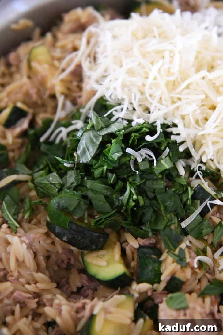 Effortless Tuna Zucchini Orzo Skillet 6 Fresh basil leaves and grated Parmesan cheese generously sprinkled over the tuna, zucchini, and orzo pasta in a stainless skillet, adding vibrant color and aroma.