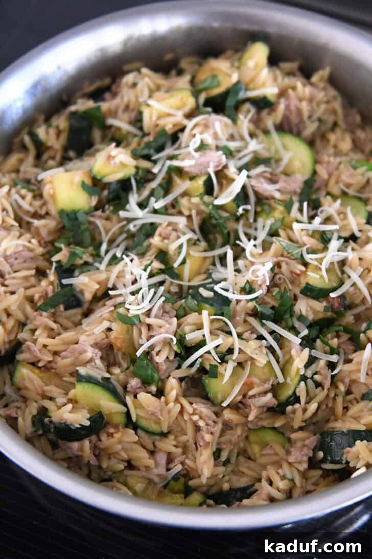 Effortless Tuna Zucchini Orzo Skillet 7 A stainless steel skillet brimming with cooked orzo, tender tuna, vibrant zucchini, fresh basil, and grated Parmesan cheese, showcasing the finished one-pan meal.