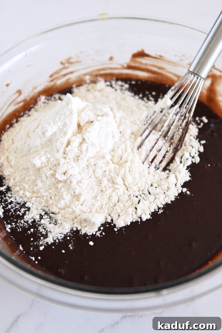 Velvety Chocolate Olive Oil Cake 8 Whisk in bowl with chocolate cake batter and white flour.