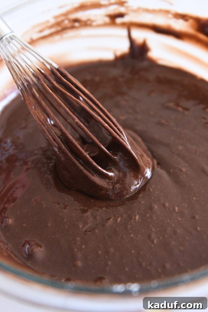 Velvety Chocolate Olive Oil Cake 9 Whisk mixing thick chocolate cake batter in white bowl.