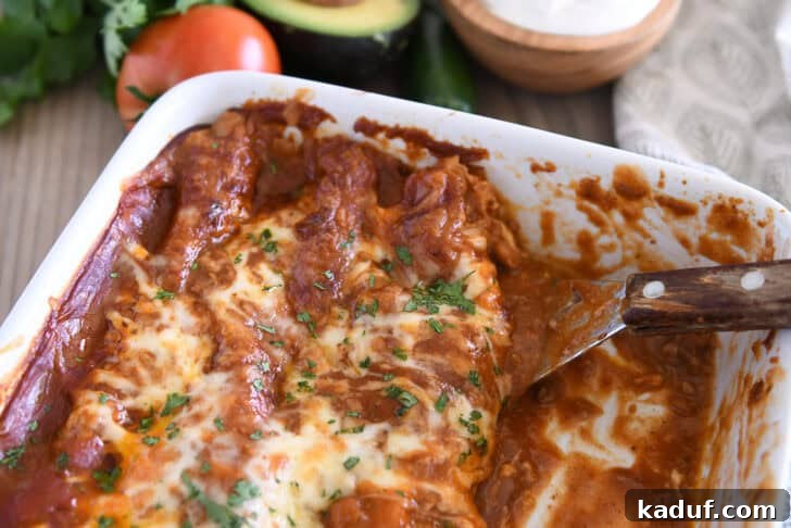 Savory Ground Beef Enchiladas 12 Square metal spatula scooping red sauce ground beef enchiladas from white 9X13-inch pan.