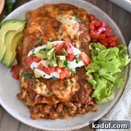 Top down view of two enchiladas on gray plate topped with red enchilada sauce, cheese, cilantro, sour cream, tomatoes, and avocados.