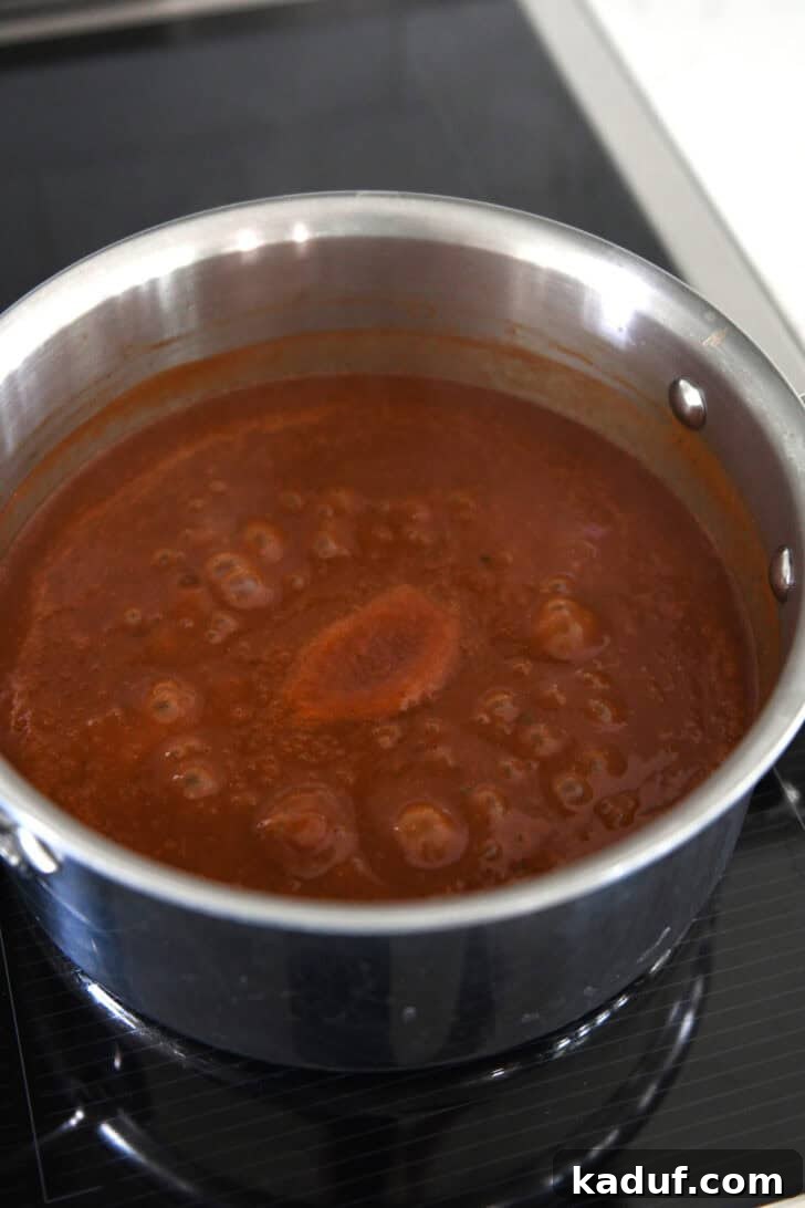 Savory Ground Beef Enchiladas 5 Homemade from-scratch red enchilada sauce simmering in stainless saucepan on induction stove.