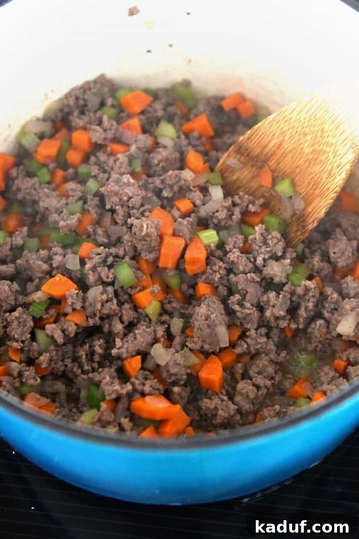 Lighter Cheeseburger Soup 3 An enameled cast iron pot contains a delicious medley of cooked ground beef, vibrant carrots, and tender celery, forming the flavorful base of the soup.