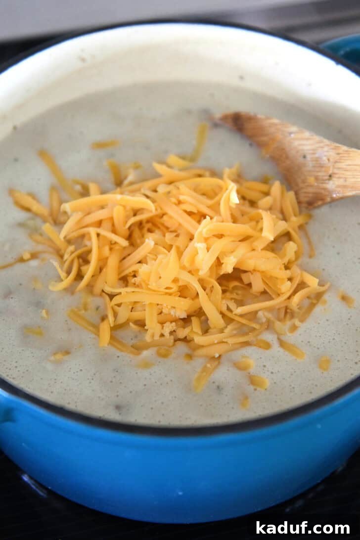 Lighter Cheeseburger Soup 4 Inside an enameled cast iron Dutch oven, a rich, creamy soup awaits, with a tempting pile of shredded sharp cheddar cheese resting in the center, ready to be stirred in.