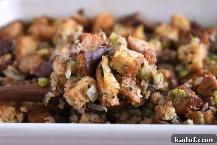 Hearty Sausage and Herb Stuffing 7 A serving spoon lifting a portion of baked sausage and herb stuffing from a pan, showing its golden-brown top.
