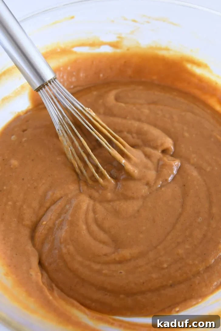 Pumpkin cupcake batter in glass bowl with wire whisk.