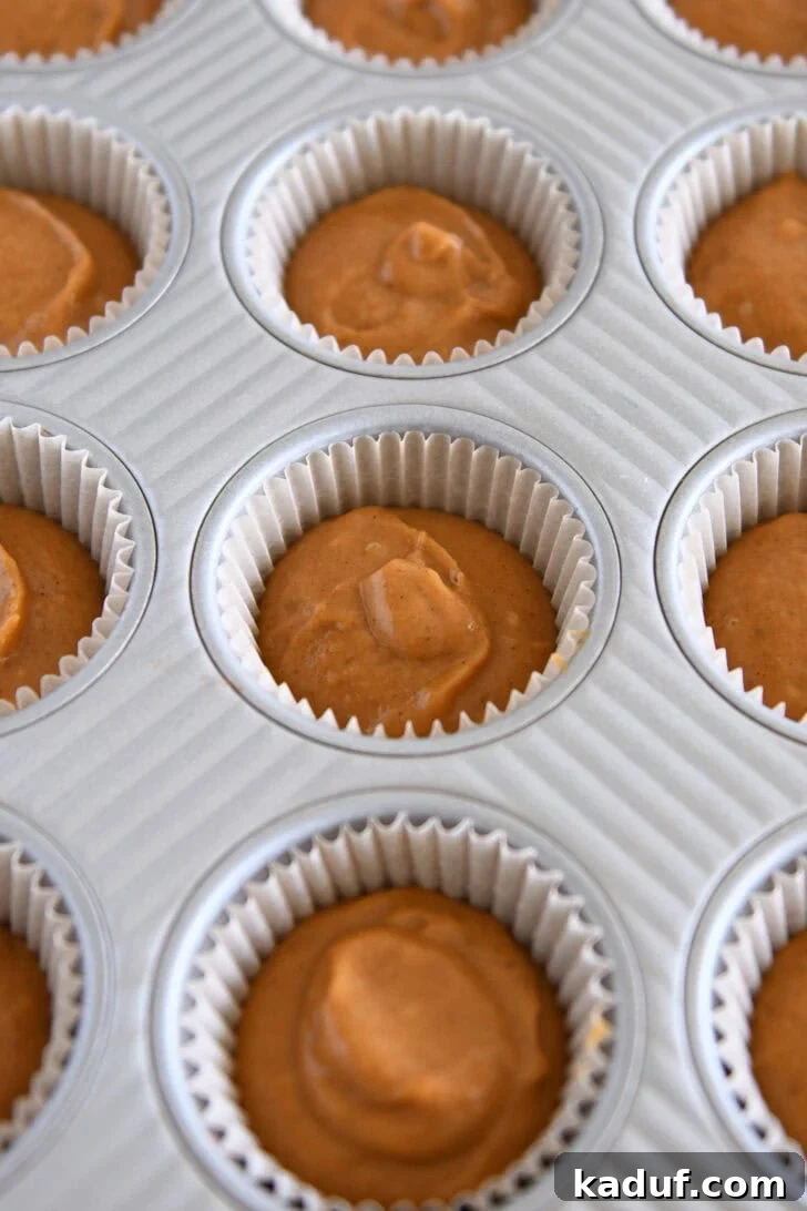Metal cupcake tin with liners filled with pumpkin cupcake batter.