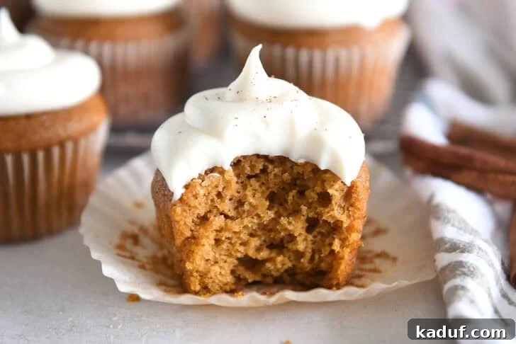 Pumpkin cupcake topped with whipped cream cheese frosting with bite taken out on unwrapped cupcake liner.