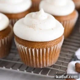 Several pumpkin cupcakes topped with whipped cream cheese frosting on wire cooling rack.