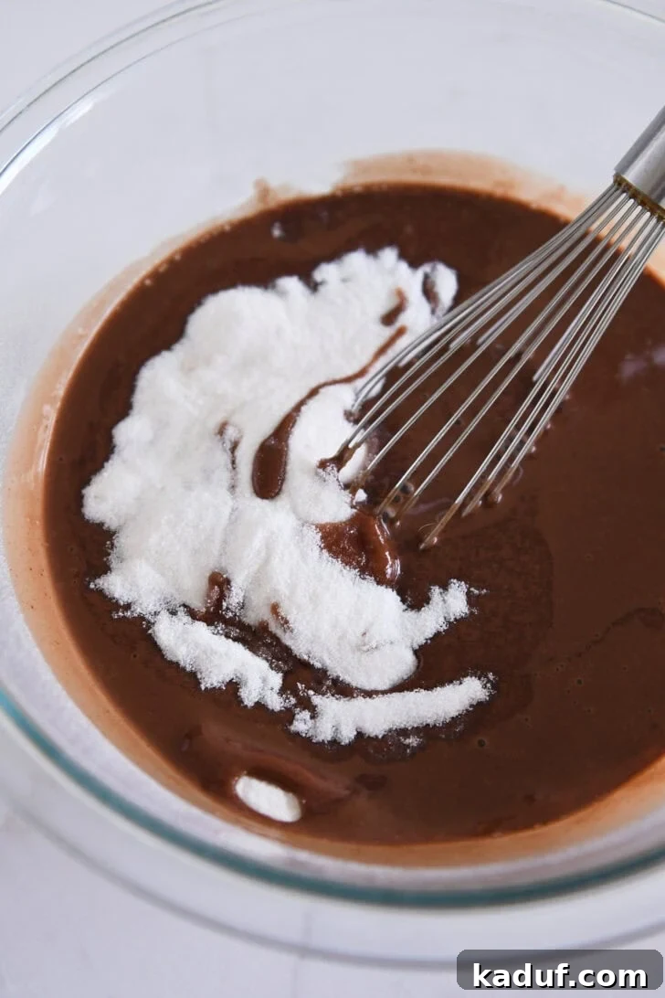 Velvet Chocolate Dream Pie 4 A glass bowl holds a rich, liquidy chocolate mixture, mixed with granulated sugar, and a wire whisk resting inside, illustrating the smooth preparation of the chess pie filling.