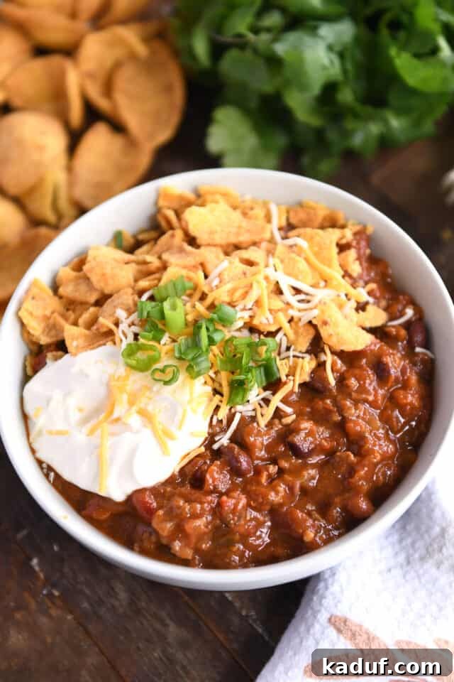 Sugarcane Spice Chili 2 Red chili with beans and ground beef in gray bowl topped with sour cream, shredded cheese, green onions, and crushed corn chips.
