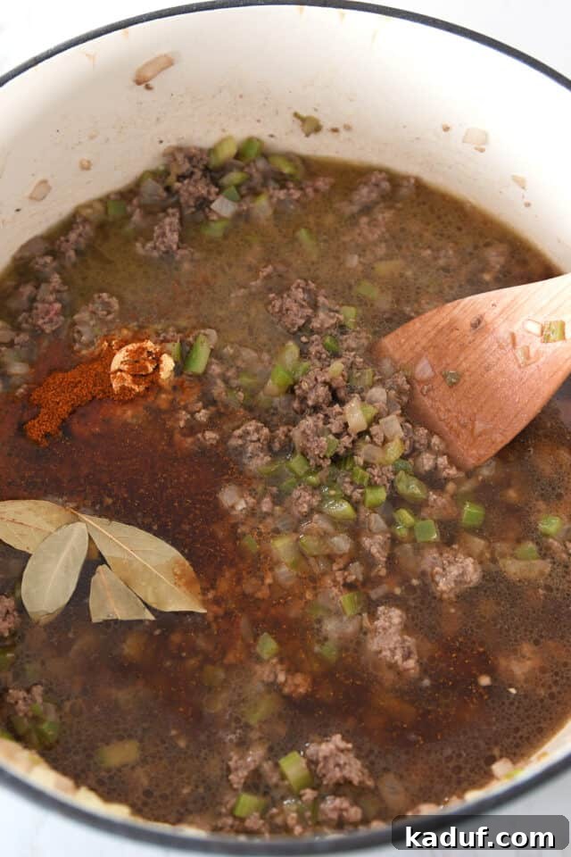 Sugarcane Spice Chili 4 Cast iron pot with cooked ground beef, chili powder, bay leaves and celery.
