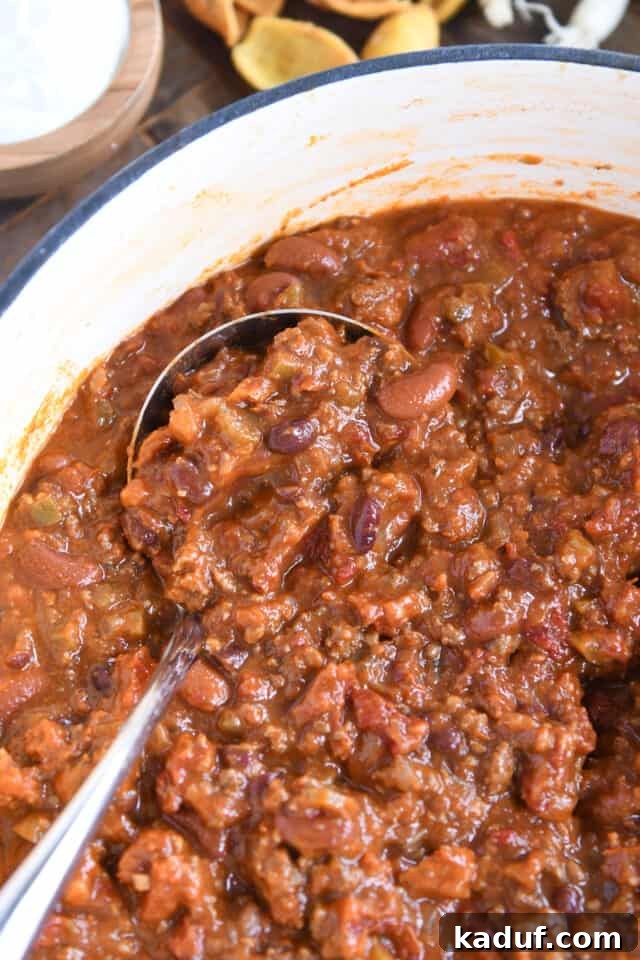 Sugarcane Spice Chili 7 Red chili with ground beef and beans in white cast iron pot with ladle.