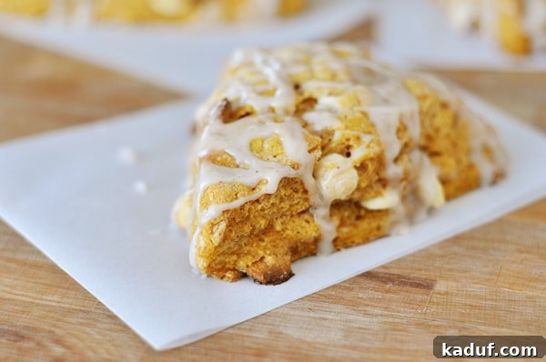 Spiced Pumpkin Scones with Ginger Drizzle 2 A perfectly glazed pumpkin scone sits on a piece of parchment paper, showcasing its tender texture and sweet ginger drizzle.