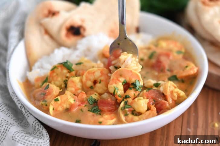 Creamy Coconut Shrimp Curry 11 A fork lifting a bite of rice and shrimp curry from a white bowl, with flatbread on the side.