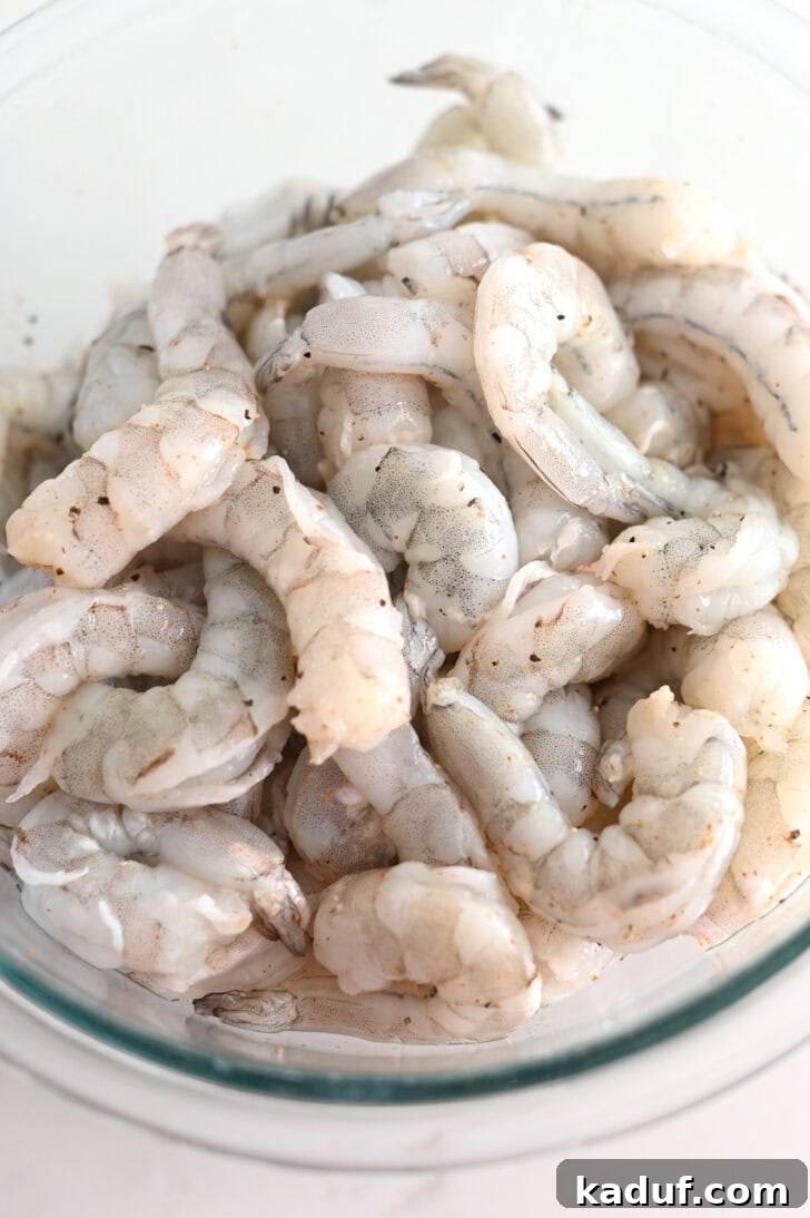 Creamy Coconut Shrimp Curry 3 Top down view of raw shrimp seasoned with spices and lemon juice in a glass bowl.