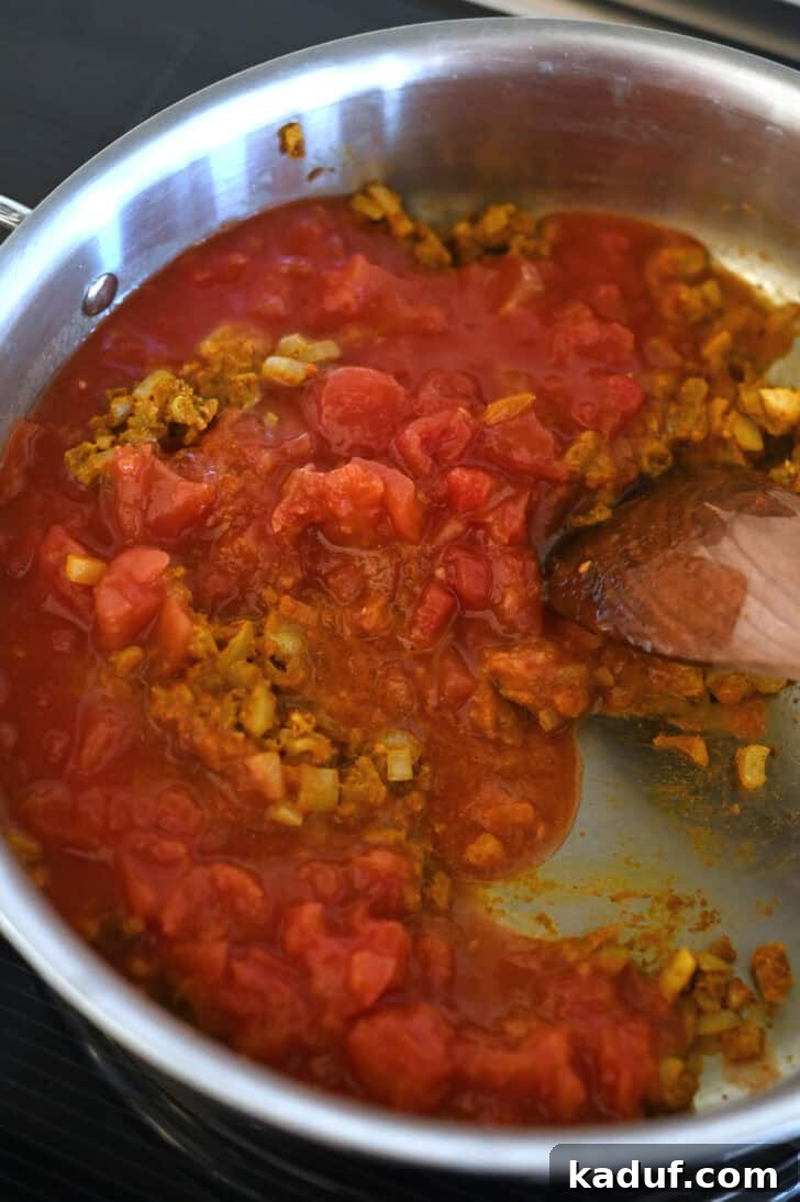 Creamy Coconut Shrimp Curry 5 Diced tomatoes, curry spices, and onions cooking together in a metal pot.