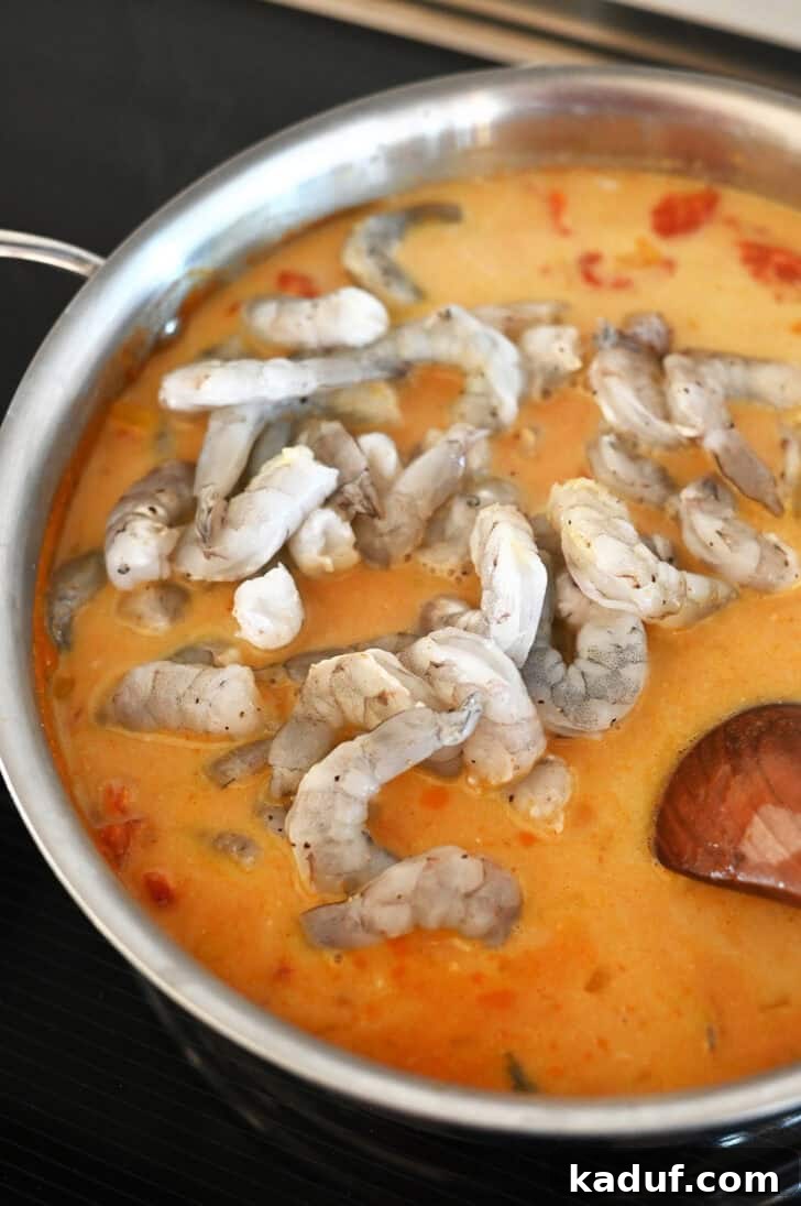 Creamy Coconut Shrimp Curry 7 Raw shrimp being added to a simmering metal pot with a rich tomato coconut curry sauce.