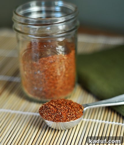 Signature Homemade Taco Blend 3 Homemade taco seasoning in a mason jar and scooped in a silver tablespoon in front of the jar. The jar is neatly labeled, and the seasoning is rich in color.