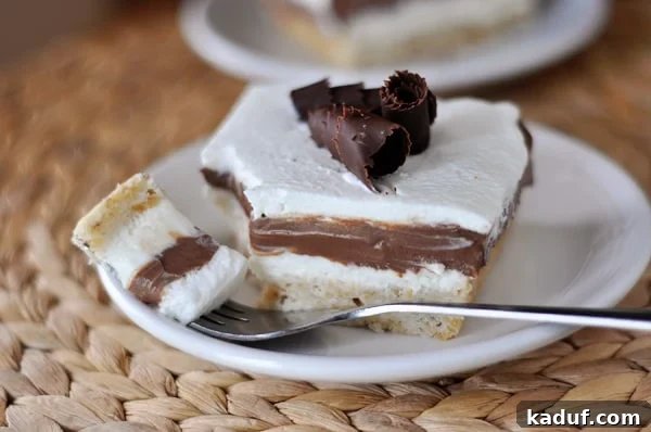 My Signature Robert Redford Dessert 2 A slice of Robert Redford Dessert on a white plate, showcasing its distinct layers: a golden shortbread crust, a light cream cheese filling, dark chocolate pudding, and a generous topping of whipped cream adorned with chocolate curls.