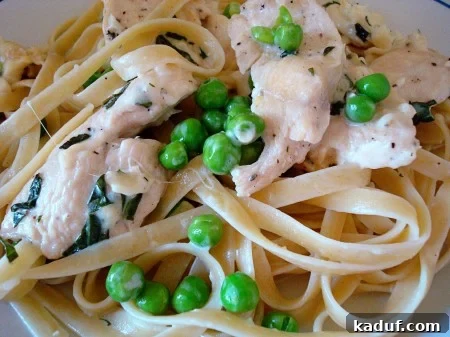 Velvety Chicken Fettuccine 2 Fettuccine noodles topped with creamy chicken and vibrant green peas, ready to be served.