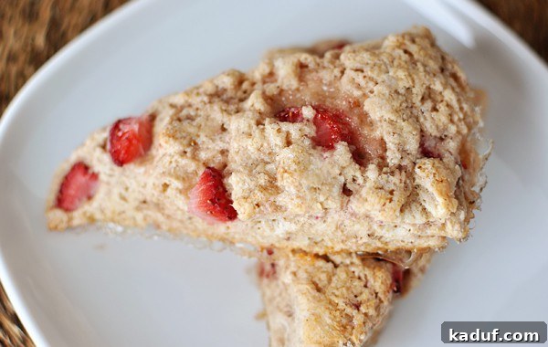 Luscious Strawberry Cream Scones 3 Top view of two strawberry-studded scones on a white plate, perfectly baked with a light glaze.
