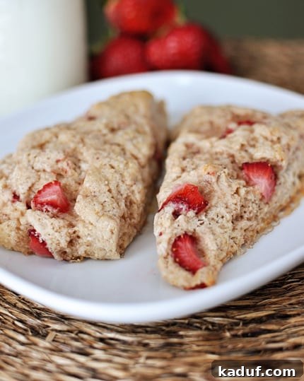 Luscious Strawberry Cream Scones 4 Two scones with pieces of strawberry laying next to each other on a white plate, highlighting the fresh fruit.