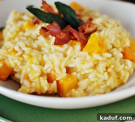 Velvety Butternut Squash Risotto 3 A close-up view of butternut squash risotto in a white bowl, generously topped with crumbled crispy bacon and fresh sage leaves, ready to be served.