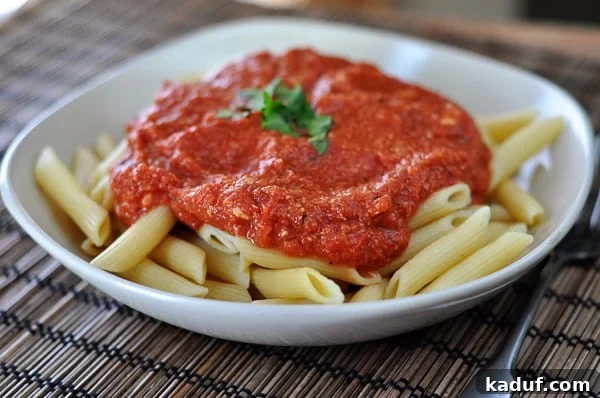 Blush Brie Pasta 3 A white bowl brimming with cooked tube pasta, generously smothered in a rich, creamy red brie sauce, ready to be enjoyed.