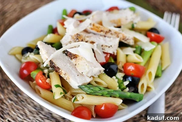 Fresh Spring Penne with Delicate Butter Sauce 3 White bowl with cooked penne pasta, pieces of asparagus, cherry tomatoes, olives, and chicken slices.