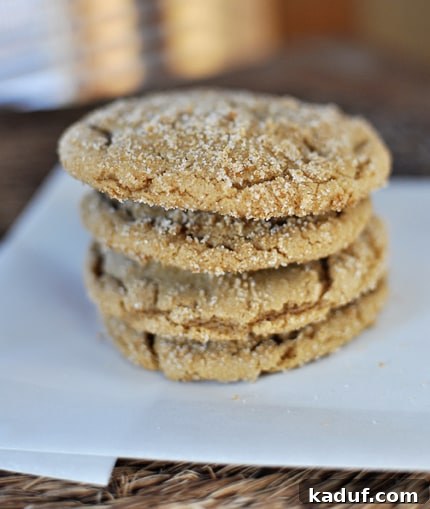 Chewy Brown Sugar Crackle Cookies 2 A stack of four sugar-coated brown sugar cookies on a piece of parchment paper, highlighting their delightful crackle tops and golden brown edges.