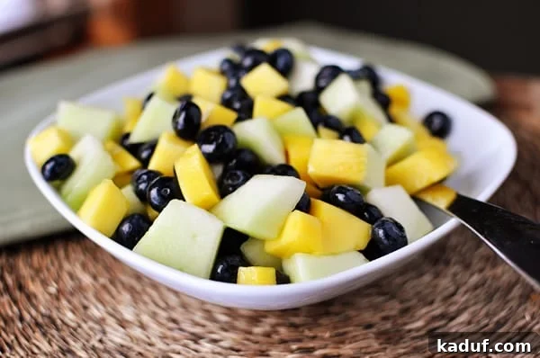 Vibrant Tropical Fruit Salad with Zesty Lime-Ginger Drizzle 2 White bowl with a honeydew, mango and blueberry salad, glistening with a syrupy glaze.
