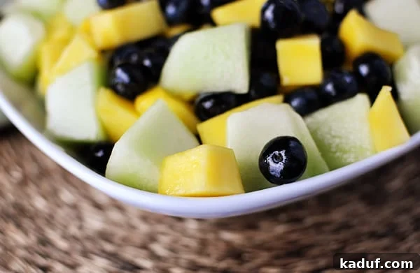 Vibrant Tropical Fruit Salad with Zesty Lime-Ginger Drizzle 3 White bowl with a closeup view of a honeydew, mango, and blueberry salad, showing the vibrant colors and glossy glaze.