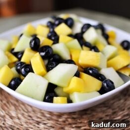 White bowl with a honeydew, mango and blueberry salad, with lime-ginger reduction