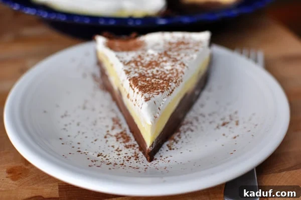 Decadent Dark Chocolate Cream Pie 2 A perfectly sliced Black Bottom Pudding Pie on a white plate, revealing distinct layers of chocolate crust, dark chocolate custard, vanilla custard, and rum-vanilla whipped cream, lightly dusted with cocoa.