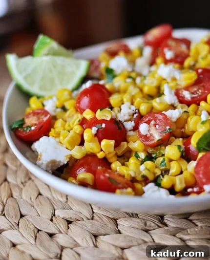 Fiesta Tomato Corn Salad 2 White bowl with corn and tomato Mexican salad with lime wedges on the side.