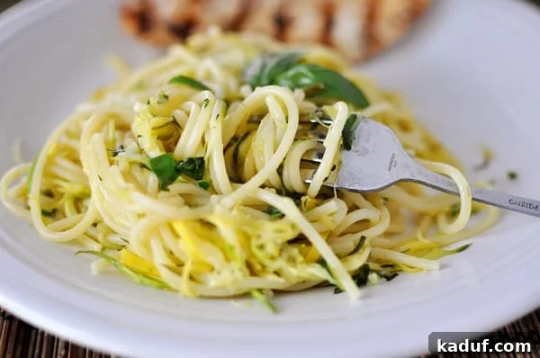 Garden Fresh Zucchini and Yellow Squash Noodles 2 White plate with linguine pasta with cooked zucchini and yellow squash in it, garnished with fresh basil.