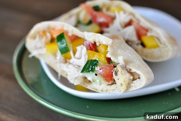 Effortless Slow Cooker Greek Chicken Pockets 2 A pita cut in half on a white plate stuffed with a greek chicken mixture.