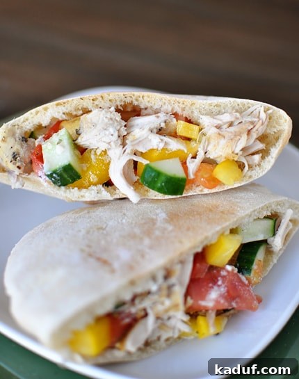 Effortless Slow Cooker Greek Chicken Pockets 3 A pita cut in half with an inside view of a greek chicken mixture stuffed inside each pita half.