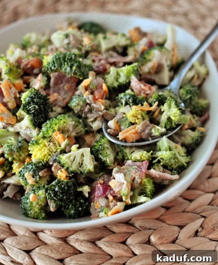 Creamy Broccoli Delight 3 A close-up view of a homemade broccoli salad with a serving spoon, highlighting the crisp broccoli florets, cheese, bacon, and sunflower seeds coated in a creamy dressing.