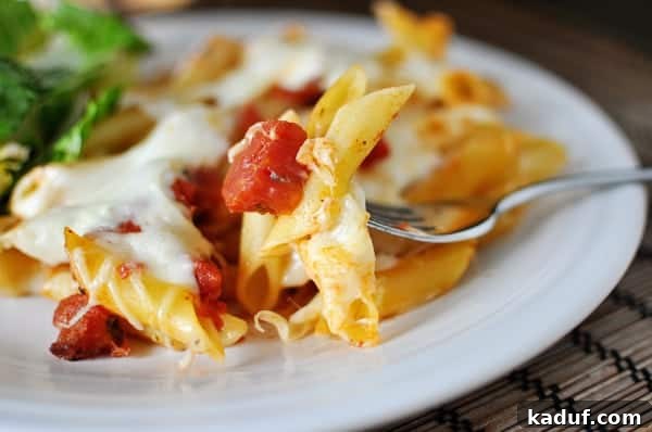 Classic Baked Pasta with Tomato and Mozzarella 2 White plate with baked cheesy pasta and tomato dices, ready to serve.