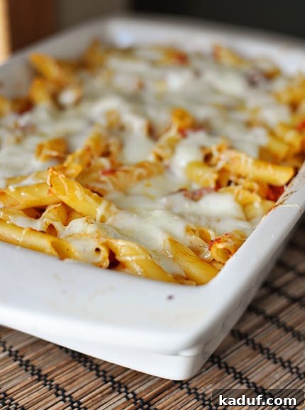 Classic Baked Pasta with Tomato and Mozzarella 3 White casserole dish full of baked cheesy pasta with melted cheese and fresh herbs.