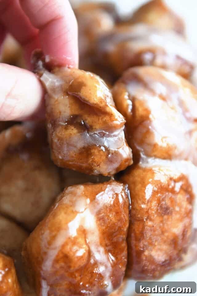 The Ultimate Sticky Pull Apart Monkey Bread 13 A hand reaches in to pick a gooey, cinnamon-sugar coated piece of monkey bread from a warm, freshly baked pile on a serving platter.