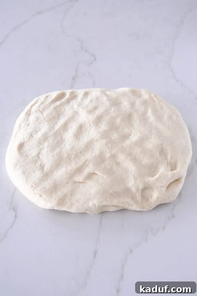 The Ultimate Sticky Pull Apart Monkey Bread 4 Smooth, elastic dough gently patted into a thick rectangular shape on a lightly floured surface, ready for cutting.