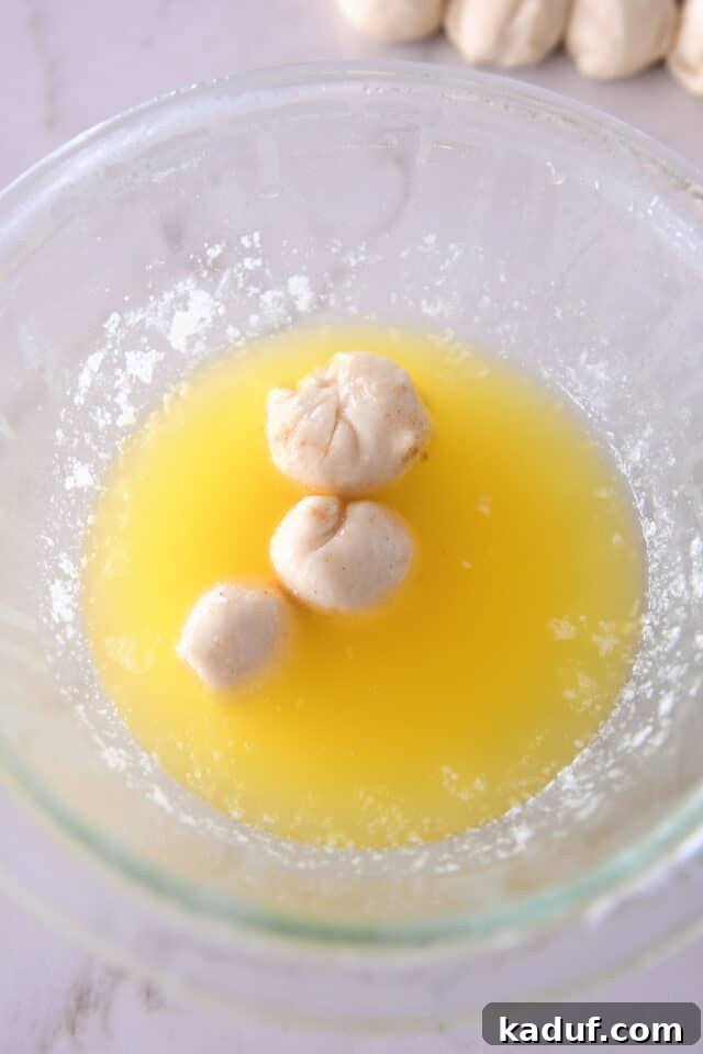 The Ultimate Sticky Pull Apart Monkey Bread 7 Small balls of dough submerged in a bowl of melted butter, ensuring full coating before rolling in sugar.