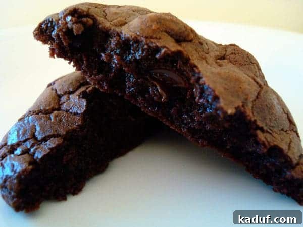Decadent Double Chocolate Chewies 2 Chocolate cookie split in half on a white plate, revealing a gooey center and melted chocolate chunks.