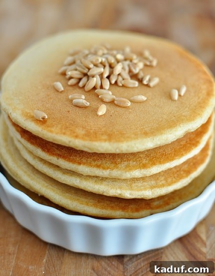 Effortless Whole Wheat Blender Pancakes 2 A stack of perfectly golden whole wheat blender pancakes, garnished with a sprinkle of fresh wheat berries, resting in a pristine white ramekin. The texture appears light and airy, promising a delightful breakfast experience.